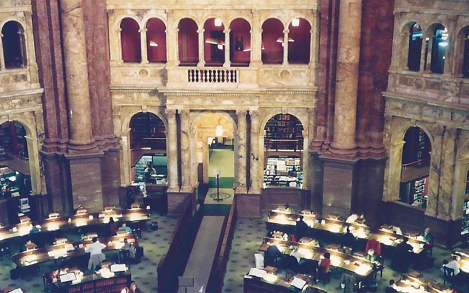 Readers sit at desks beneath ornate marble arches in a grand library reading room