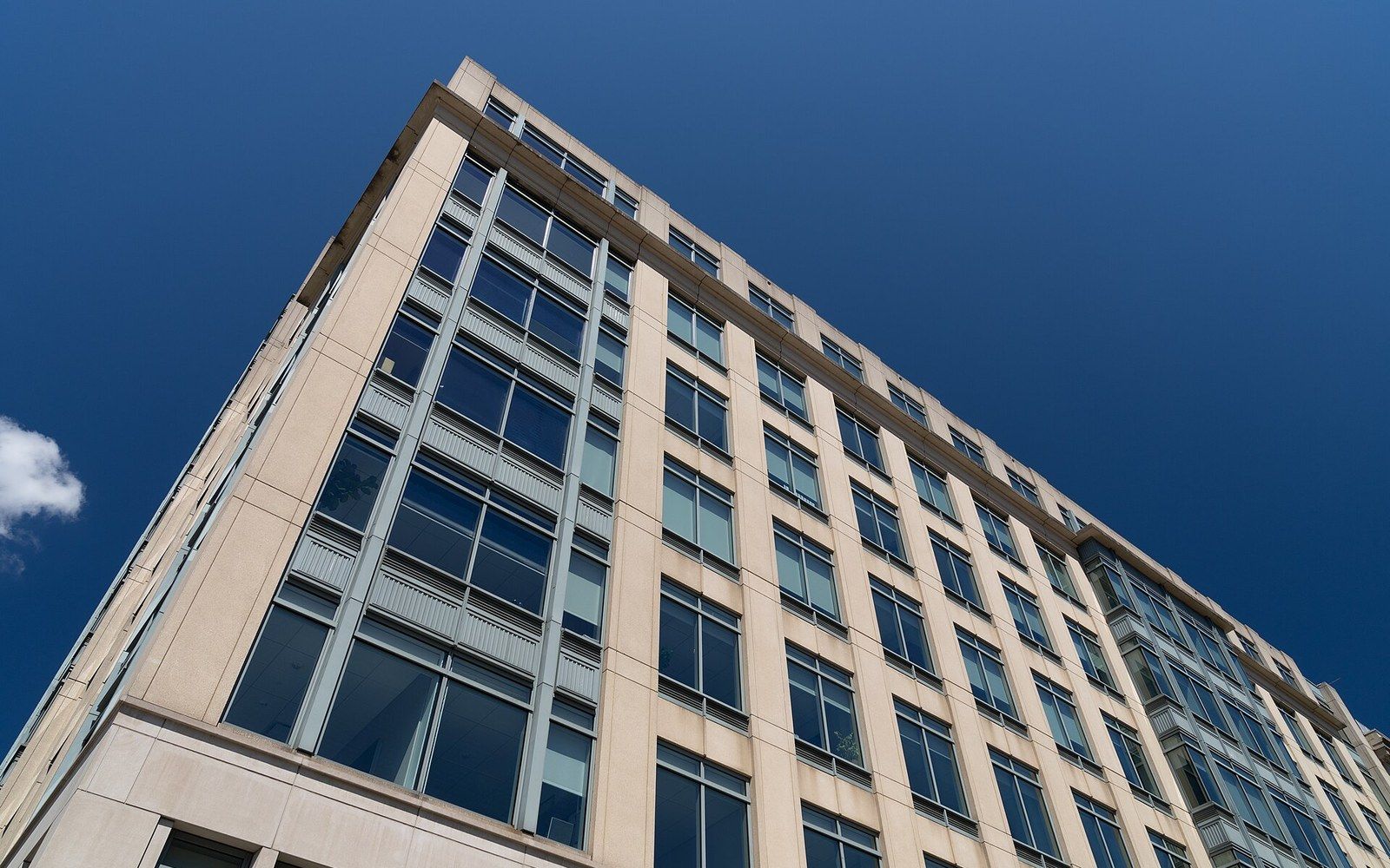 Upward view of a tan office building's corner facade against a clear blue sky