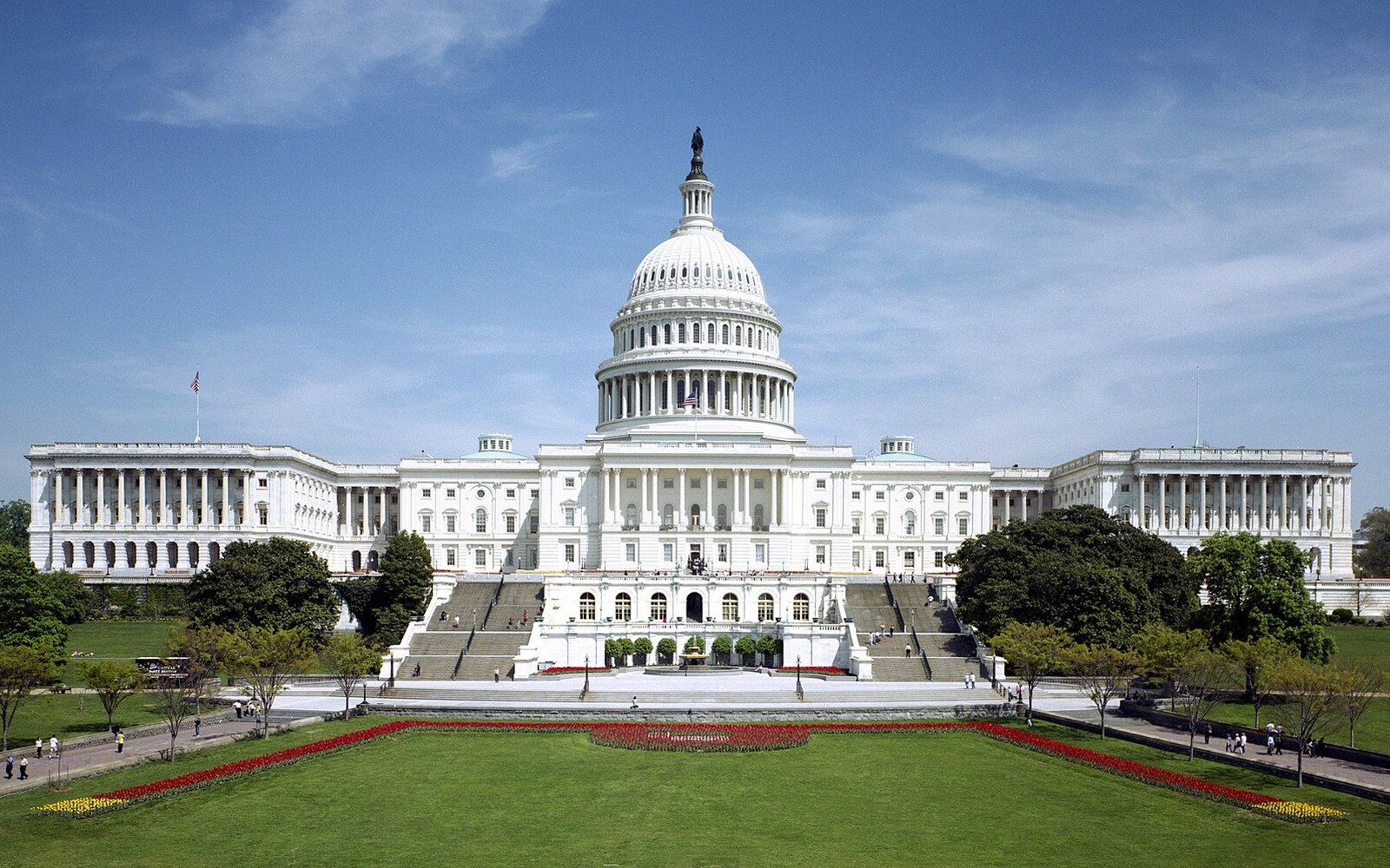 The US Capitol building's dome and east facade seen across manicured lawns and flower beds