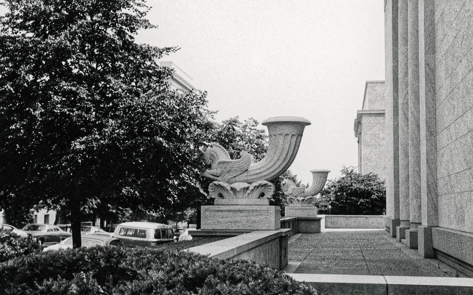 Ornate carved horn sculptures flank a colonnaded building entrance along a tree-lined street