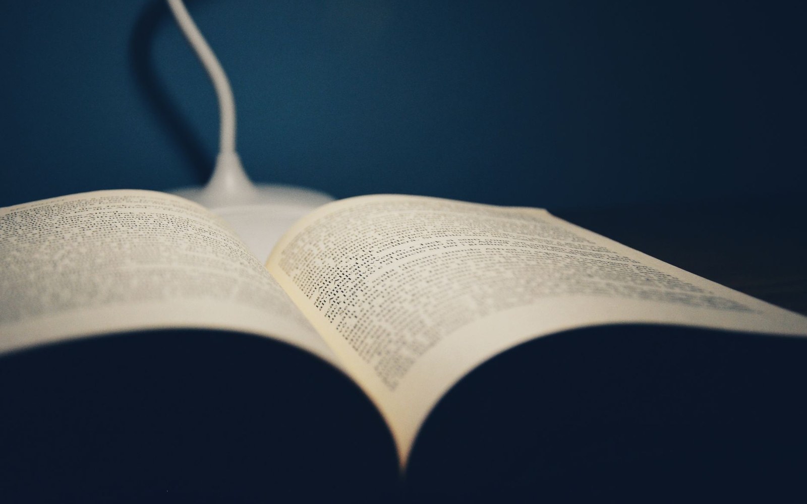 An open book with dense text lit by a small desk lamp