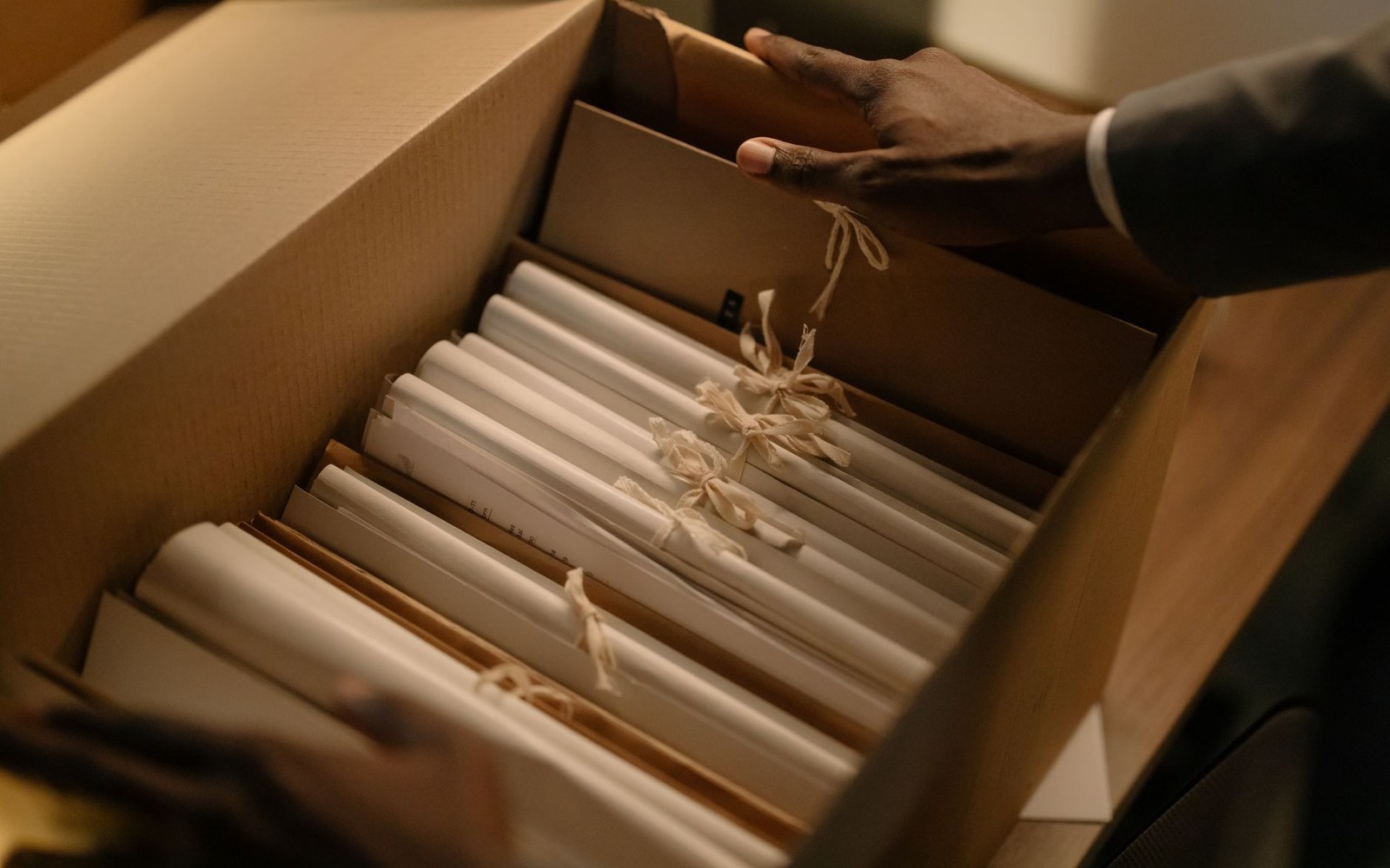 Hands open a cardboard box holding legal document folders tied with string