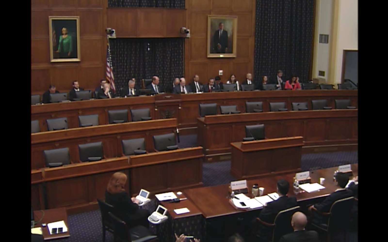 Committee members sit at a raised dais during a congressional hearing in wood-paneled room